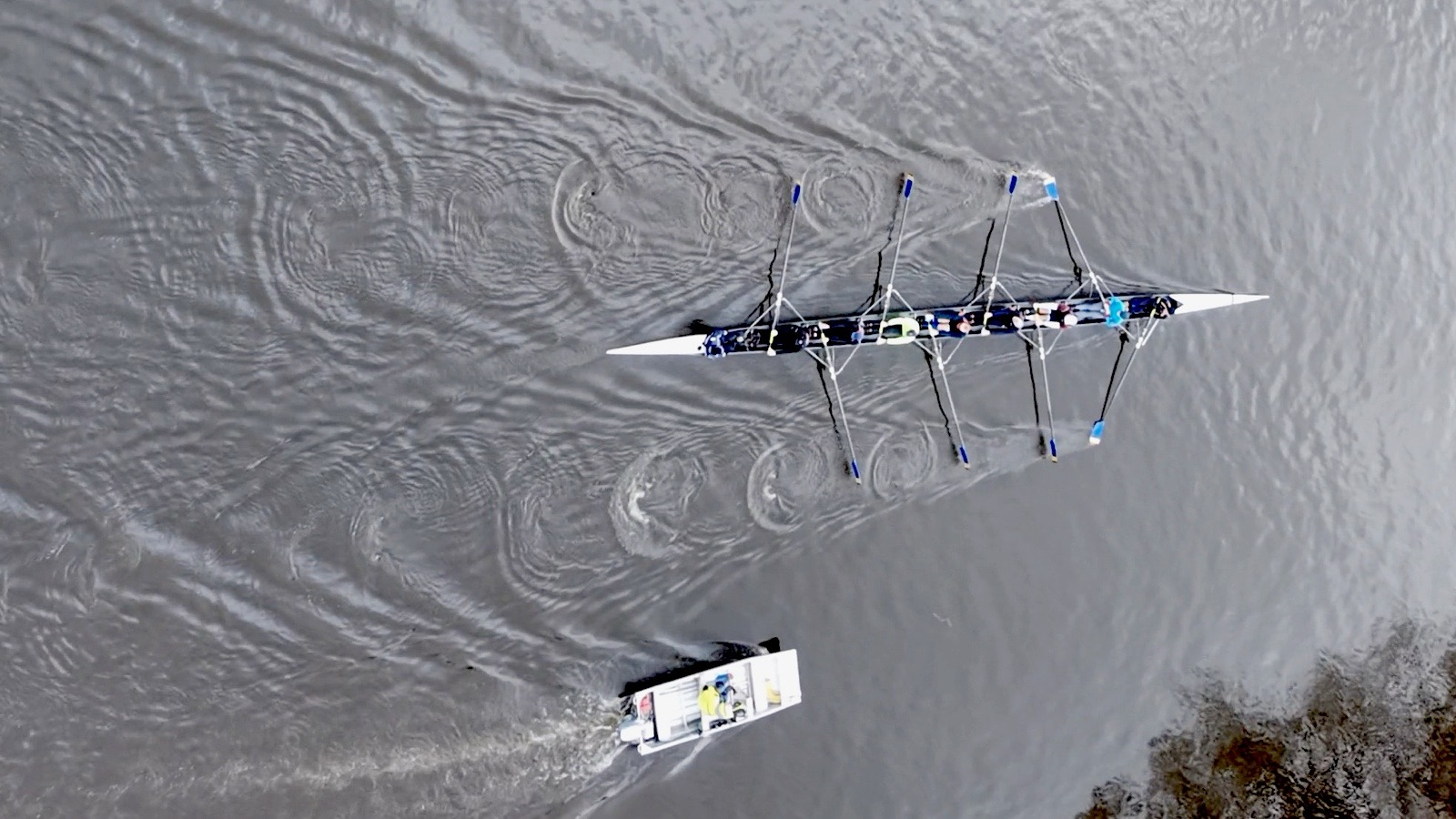 An eight seen from above on a river, blades in the water, with the coach launch behind